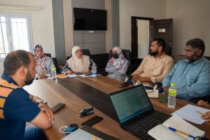 WhatsApp Image 2026-05-14 at 12.06.33 PM - جامعة سبها | Sebha University Seven people in a conference room around a wooden table, with laptops, notebooks, and water bottles, in a discussion.