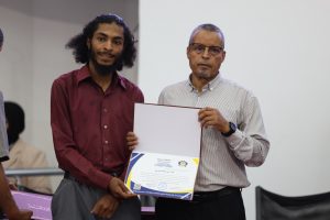 Two men pose with a large certificate during an awards ceremony, facing the camera.