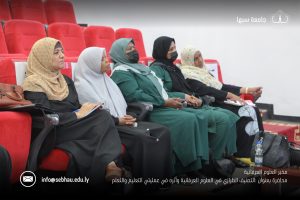 Group of five women wearing hijabs seated in red theater-style chairs, some with face masks, attending a lecture or presentation.