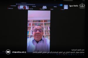 Video conference screen showing a speaker in a library background with bookshelves, Arabic text, and institutional logos at the edges.