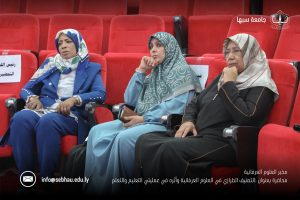 Three women in hijabs sit in red auditorium seats, listening attentively at a conference.