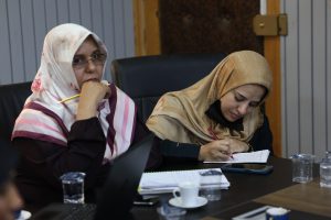WhatsApp Image 2026-05-20 at 10.03.09 AM (1) - جامعة سبها | Sebha University Two women in headscarves sit at a conference table, one writing in a notebook while the other looks on pensively.