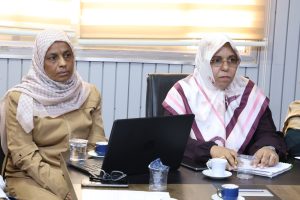 WhatsApp Image 2026-05-20 at 10.03.10 AM - جامعة سبها | Sebha University Two women wearing patterned hijabs sit at a conference table with laptops, cups, and papers in front of them during a meeting.