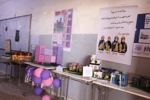 Exhibition display: posters on a wall, miniature building models on tables, and purple balloons decorating the scene.