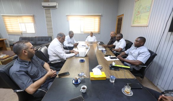 1092713C-F10C-4331-8F1E-2C8AB7780C6E - جامعة سبها | Sebha University Group of men in business attire seated around a long conference table in a meeting room, with laptops and coffee cups.