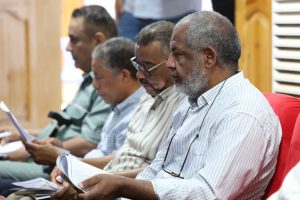 1D1C4A87-1955-46B0-A711-FDA70FC0C06C - جامعة سبها | Sebha University Group of men seated in a row, reading papers during a meeting.