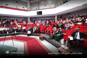 Audience seated in red chairs inside a large lecture hall during an academic conference.