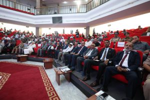 46EA660F-1348-4316-9AB7-2CB4081D9C9C - جامعة سبها | Sebha University Large audience seated in red theater-style seats for a formal conference in a spacious auditorium.