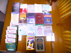 Row of Arabic-language books spread out on a wooden table, showing colorful covers.
