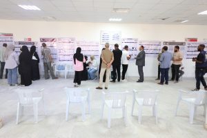 Group of people viewing large posters displayed along a wall at a poster session in a bright hall.