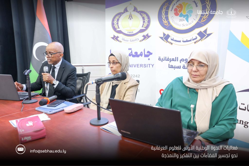 Panelists seated at a table with microphones and laptops during a university event, banners with logos in the background.