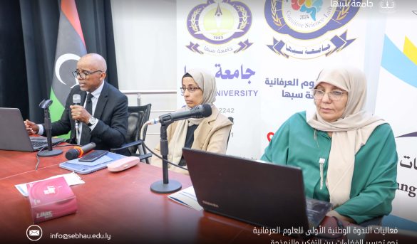 Panelists seated at a table with microphones and laptops during a university event, banners with logos in the background.
