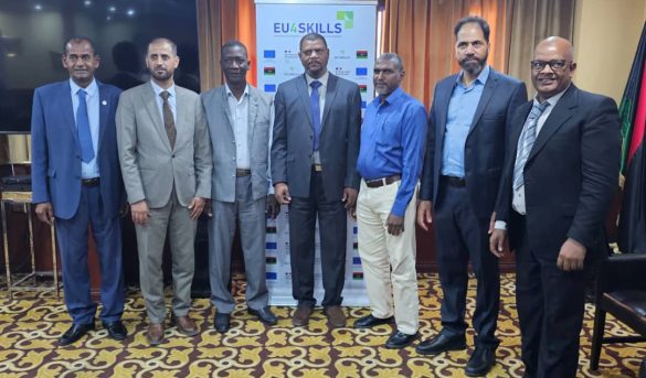 Seven men in suits standing in a row at an EU4Skills event, posing for a group photo indoors in front of a banner.