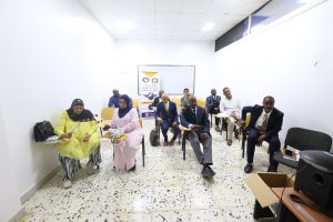 610348E8-B7A7-43FD-8EC8-77140826AC28 - جامعة سبها | Sebha University A small group of adults seated in a bright classroom, some taking notes, with a banner and whiteboard at the back.