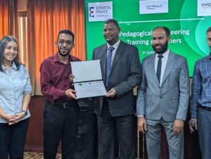 652E4331-4EB8-4794-9A2F-C87872EC6CA4 - جامعة سبها | Sebha University Six professionals pose at an awards ceremony as a man in a maroon shirt receives a certificate from a taller man in a suit, with a green event banner in the background.