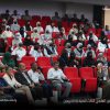 Audience seated in red theater chairs at a conference, many attendees wearing masks, front row with men in suits and women in traditional dress.