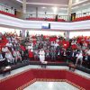 Wide view of a formal conference hall filled with attendees seated in red chairs on multiple tiers.