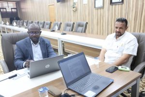 B0062CF4-6A7A-4B94-BA03-03F846139A34 - جامعة سبها | Sebha University Two men sit at a long conference table with laptops in a formal meeting room.
