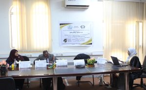 People seated around a conference table in a bright room, with a poster on the wall behind them.