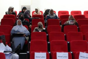 E47A7856-6C3B-4176-8240-F3D69FBB5C85 - جامعة سبها | Sebha University Group of women wearing hijabs seated in red auditorium chairs, some with masks, at a meeting or conference in progress.