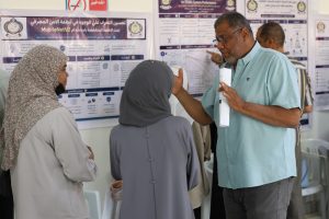 Medical staff and visitors discuss health posters on a wall in a clinic or lab setting; man holds a rolled poster.