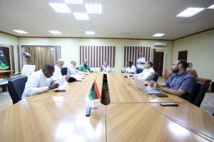 Team of professionals around a large conference table reviewing documents in a meeting room with Libyan flags on the table center.