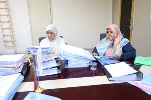 WhatsApp Image 2026-06-02 at 12.45.50 PM - جامعة سبها | Sebha University Two women wearing hijabs sit at a cluttered desk filled with papers, reviewing documents at a busy office table.