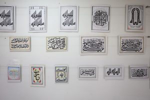 WhatsApp Image 2026-06-14 at 12.43.20 PM (1) - جامعة سبها | Sebha University Gallery wall displaying multiple framed Arabic calligraphy artworks in two rows on a white surface.