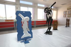WhatsApp Image 2026-06-14 at 12.43.21 PM (2) - جامعة سبها | Sebha University Blue abstract metal sculpture of a standing figure with cutout shapes, placed on a white surface in a bright gallery.