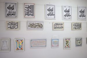 WhatsApp Image 2026-06-14 at 12.43.21 PM - جامعة سبها | Sebha University Row of framed Arabic calligraphy prints hang on a white gallery wall, varying border designs and orientations on display.