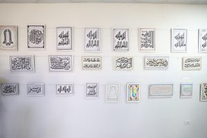 WhatsApp Image 2026-06-14 at 12.43.23 PM (3) - جامعة سبها | Sebha University Row of framed Arabic calligraphy artworks hung on a white gallery wall in a single row.