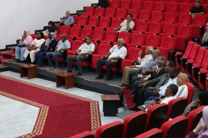WhatsApp Image 2026-06-14 at 12.45.24 PM - جامعة سبها | Sebha University Audience members seated in red theater seats watching an event in a conference hall, front row with several men and women.