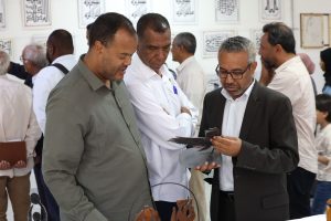 WhatsApp Image 2026-06-14 at 12.45.25 PM (1) - جامعة سبها | Sebha University Group of men at an art gallery examining metal bird sculptures on display behind them, wall-mounted artworks visible in the background.