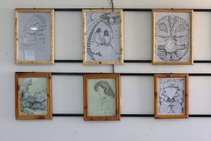 WhatsApp Image 2026-06-14 at 12.45.26 PM - جامعة سبها | Sebha University Framed pencil drawings along a wall: left a carved-wood head, middle an abstract scene with two figures, right a circular ornamental pattern.
