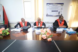 Three men in black academic robes with red sashes sit at a conference table during a formal meeting, with a poster on the wall behind them.