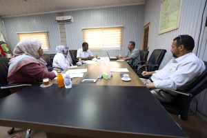 Six professionals seated around a conference table in a meeting room, reviewing documents and notes.