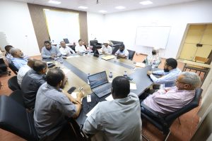 Group of professionals seated around a large conference table in a meeting room, laptops and water bottles on the table.