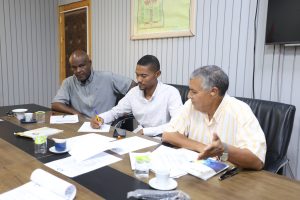 4E68F837-6D66-43E5-9943-8A9083B25B2C - جامعة سبها | Sebha University Three men in a meeting around a conference table, reviewing documents and taking notes.