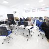 Computer lab with desks, monitors, and blue chairs as people work at desktop PCs in a bright, white room.