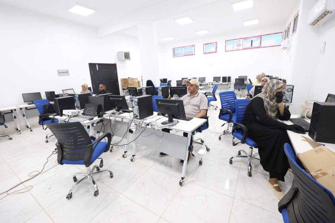 Computer lab with desks, monitors, and blue chairs as people work at desktop PCs in a bright, white room.