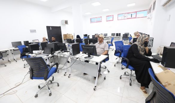 Computer lab with desks, monitors, and blue chairs as people work at desktop PCs in a bright, white room.