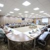 Large conference room with a U-shaped table setup and 20+ attendees discussing, flags and a SEIBA University banner in the background.