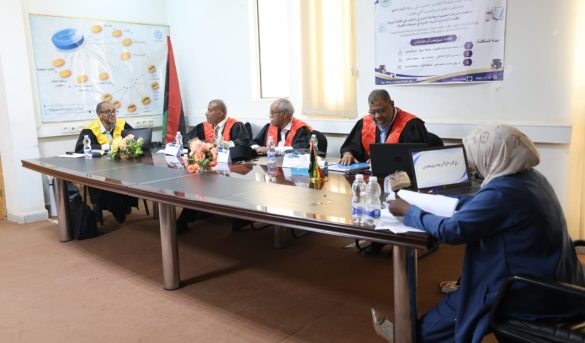 Formal panel meeting around a long table with five people in robes, banner on the wall, and flag in the corner.