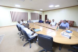 Group of people seated around a large conference table in a meeting room, discussing or reviewing documents.
