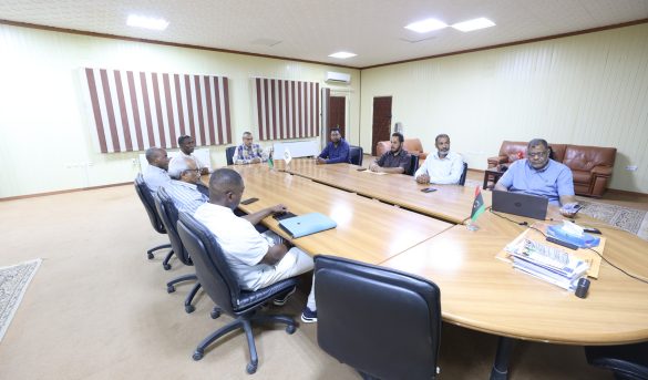 Group of people seated around a large conference table in a meeting room, discussing or reviewing documents.