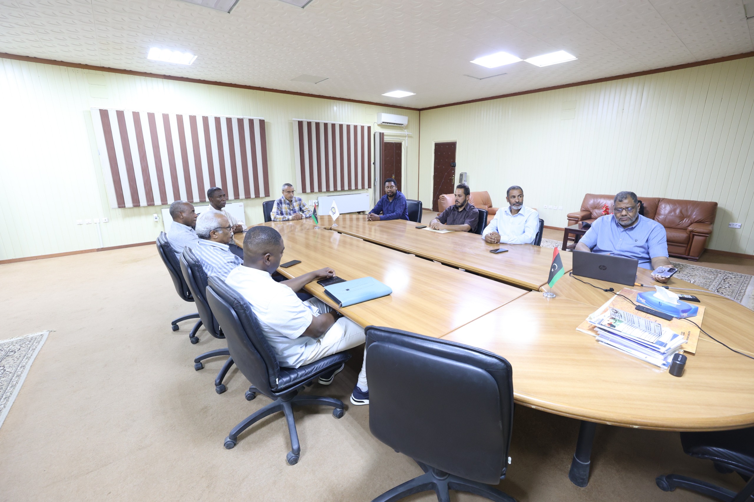 Group of people seated around a large conference table in a meeting room, discussing or reviewing documents.