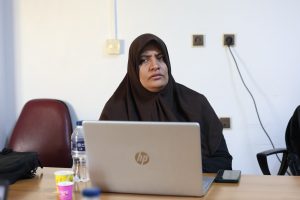 A60BF661-5FE1-44D6-8C69-D228FDF3BE53 - جامعة سبها | Sebha University Woman in a dark hijab seated at a desk, working on an HP laptop with a bottle and cups on the table nearby.