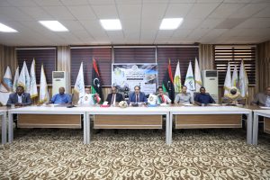 D5B61226-168F-4515-9158-5292B79C1780 - جامعة سبها | Sebha University Officials seated at a long conference table with national and organizational flags behind them in a formal meeting room.