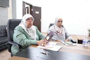 F0450214-F379-4AAE-A46C-09C490EAE769 - جامعة سبها | Sebha University Two women wearing hijabs sit at a conference table, reviewing documents and notes in a meeting room.
