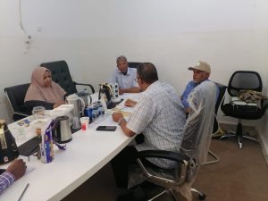 People sit around a white table in a meeting room, with snacks and coffee on the table.